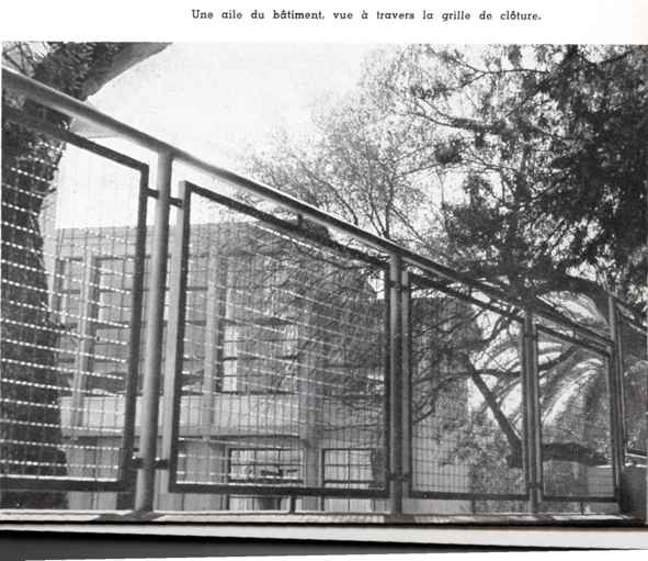 Une aile du bâtiment, vue à travers la grille de clôture. 