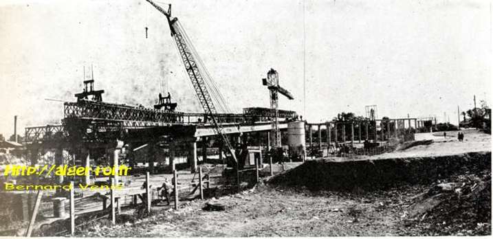 Une vue générale du chantier implanté dans la zone du marché à bestiaux. Pose de poutres préfabriquées (hauteur sous tablier 5 m 50 environ). A g,: on aperçoit la berge opposée de l'oued Harrach. Au fond à dr.: le passage à niveau (rue de France) de la voie ferrée Alger-Constantine. 